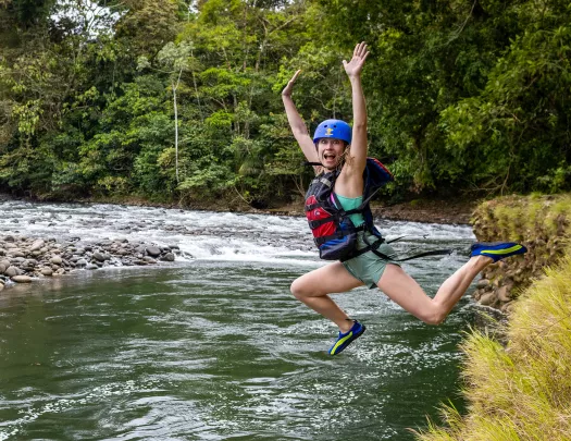Woman wearing a helmet and life vest jumping into a lake