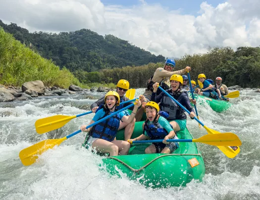 Two groups of families on green rafts, paddling in a river