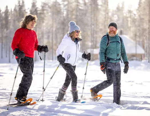 Women and two men with hiking poles and snow shoes, walking in a valley of snow