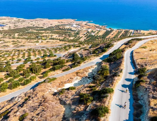 Long, empty roads with people biking, with the ocean in the distance