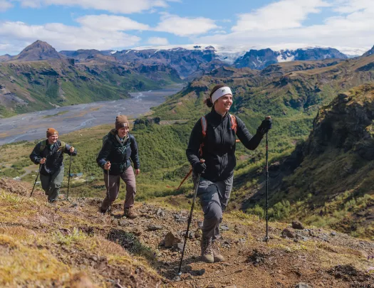 Group of three people with hiking poles, walking on a dirt and gravel trail on a hill