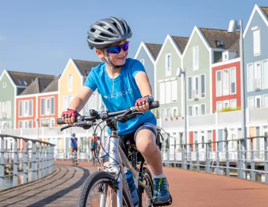 Boy smiling while riding a bike on a bridge, with rows of colorful houses in the background