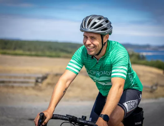 Man wearing green biking gear, smiling while biking on an empty road