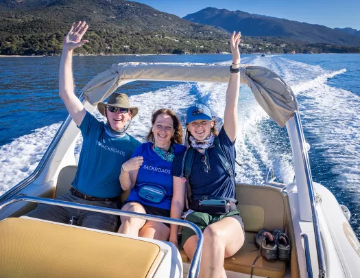 Three Backroads guests put their hands in the air on the back of a boat