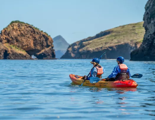 Two people paddling on an orange kayak in the middle of a lake