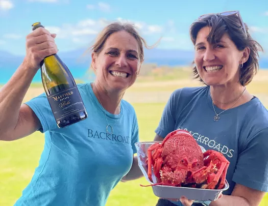 Two women smiling while holding a bottle of wine and a cooked lobster