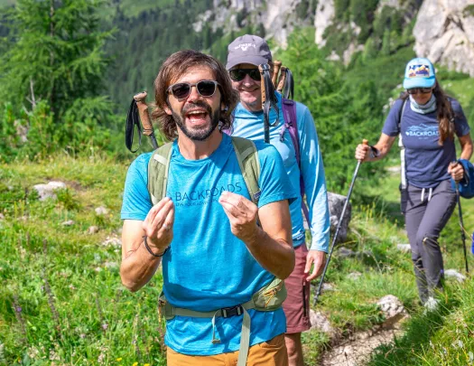 Two men and one woman walking on a trail with grassy hills in the background