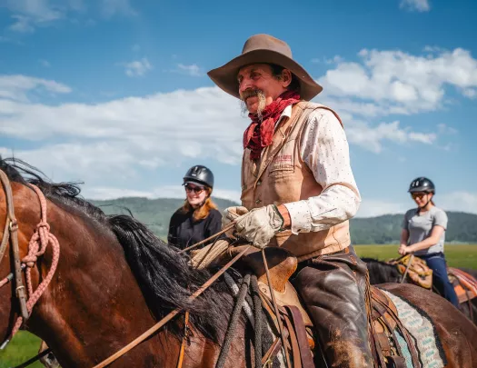 Man with cowboy gear and a long beard horseback riding