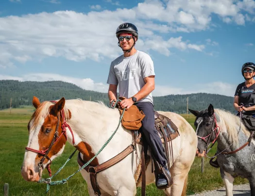 Man wearing sunglasses and a helmet, riding on the back of a horse