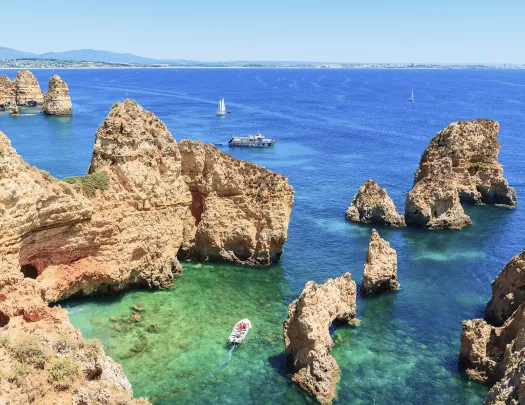 A boat navigating through large cliffs at the edge of the ocean