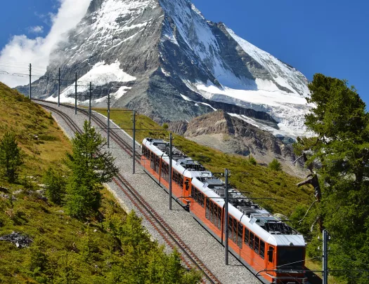 Train going down a hill, with snow-capped mountains in the distance