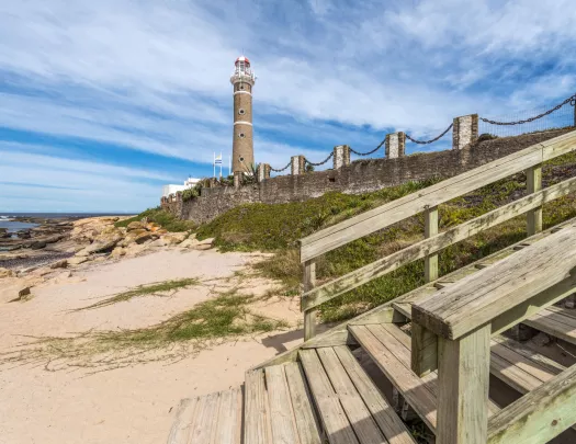 Beach with a wooden staircase and a lighthouse in the background