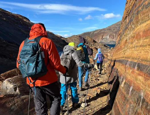 Group of people with hiking poles, walking on gravel trails along a mountain