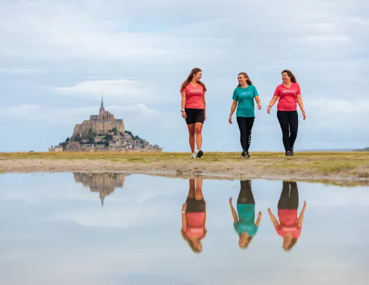 Three women walking on an empty valley, with a large castle in the distance