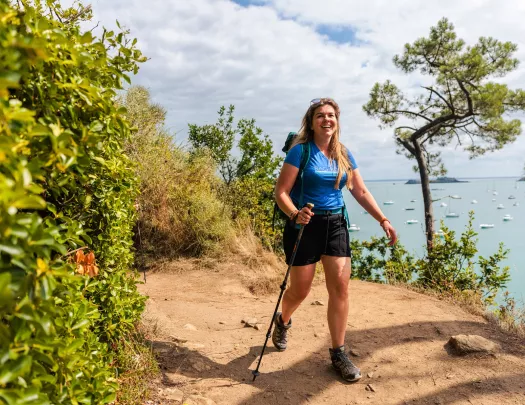 Woman walking on a dirt trail with the ocean in the background