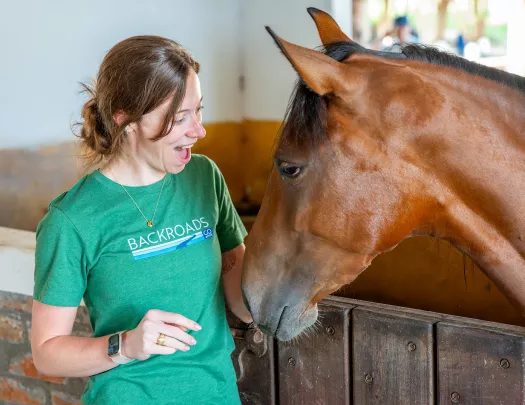 Woman in a green shirt, smiling while petting a horse
