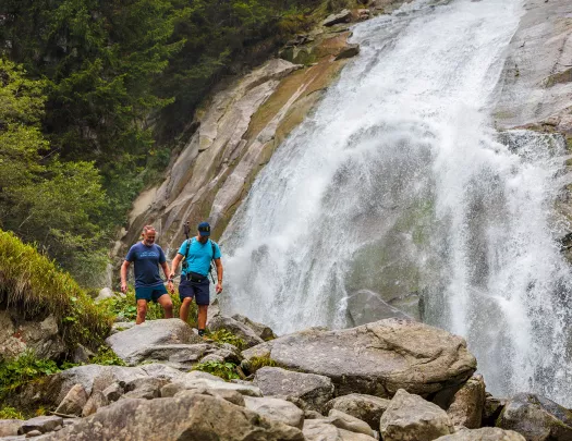 Two men hiking on a rocky trail next to a waterfall