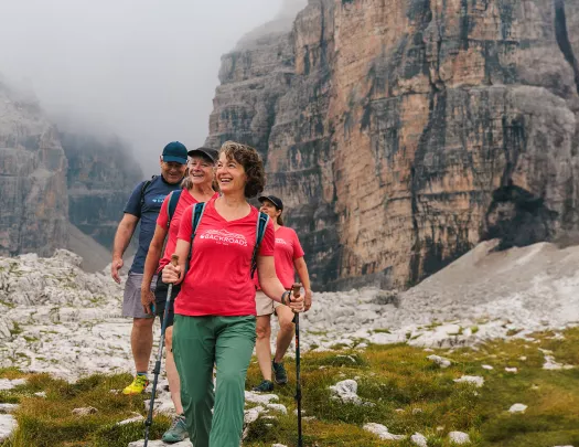 Three women and one man hiking on a grassy trail with fog-covered mountains in the background