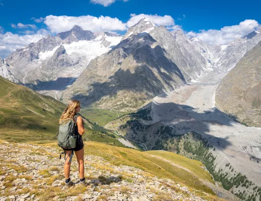 Woman wearing a backpack, looking out to a large valley of mountains and trees