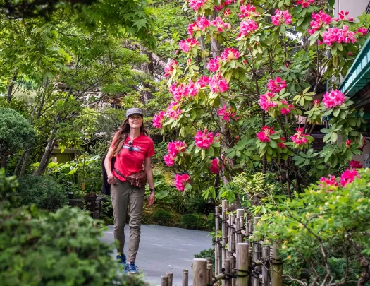 Woman smiling while walking through an outdoor garden full of plants and pink flowers