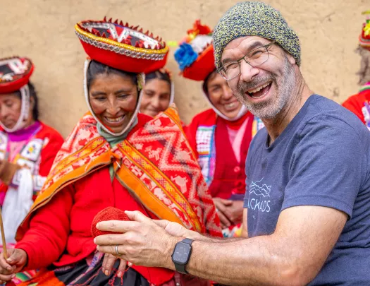 Man smiling while holding a ball of yarn, next to a woman wearing traditional attire