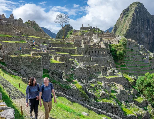 Man and woman smiling while walking on a stone path, with Machu Picchu in the background