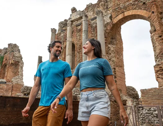 Man and woman smiling while looking at each other, with a large stone arch in the background