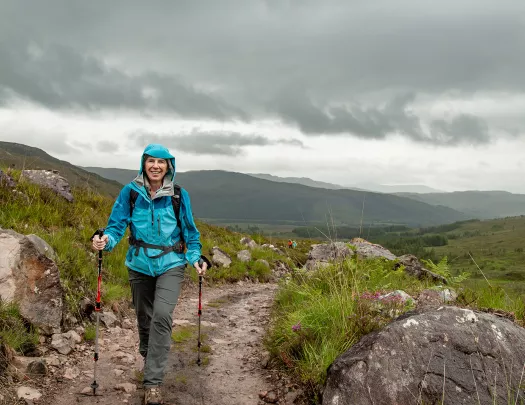 Woman wearing a blue raincoat, hiking on a dirt trail