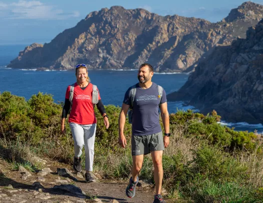 Man and woman smiling while walking on a dirt and stone path and the ocean in the background