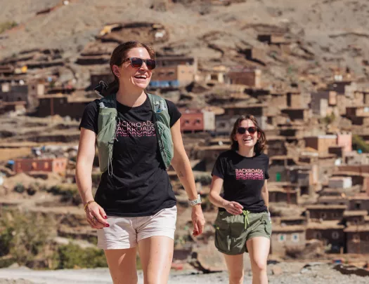 Two women smiling and walking with a town in the background