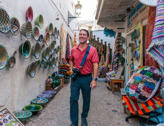 Man standing in an alleyway, surrounded by baskets and pots on the walls