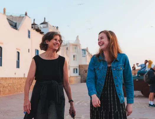Two women smiling while walking in front of a large, white building
