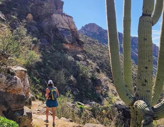 Woman hiking on a trail in the desert, surrounded by cliffs and cacti
