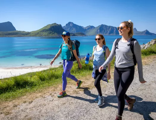 Three women walking on a dirt trail with a large lake in the background