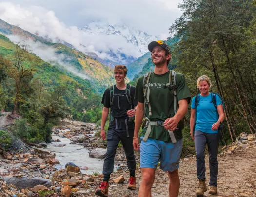 Two men and one woman walking along a frozen river with a forest in the background
