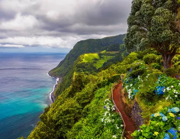 View of flowers on a mountain and the ocean in Miradouro da Ponta do Sossego Nordeste, Sao Miguel, Azores, Portugal. 