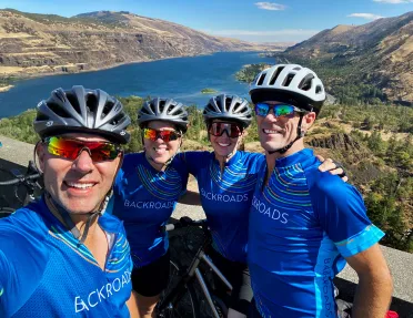 Four guests posing in front of large river/reservoir. 