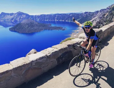 Guest cycling and gesturing towards Crater Lake on her right.