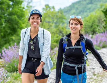 Two hikers on a trail with wildflowers.