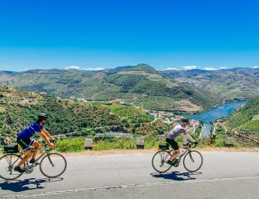 Two bikers riding on a road along the Douro River.