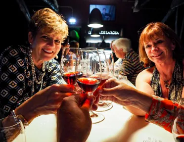 People saying cheers with glasses of red wine.