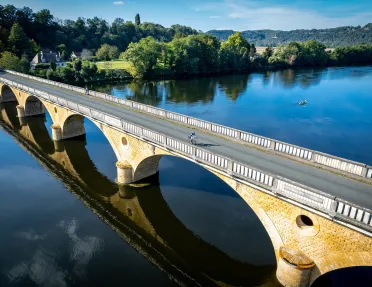 Two guests cycling on bridge, forest, meadow behind them.