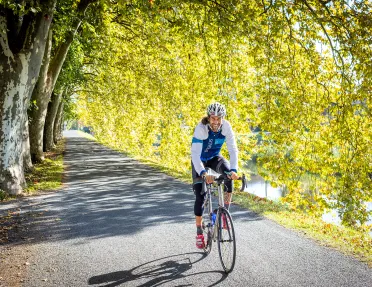 Guest/leader cycling down tree-covered road, smiling.