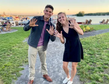Two guests waving and posing for camera, lake and boats in bakcground.