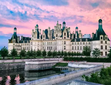 Wide shot of the Château de Chambord, purple sunset behind.