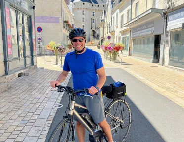 Guest with bike, standing in French road among white buildings and storefronts.