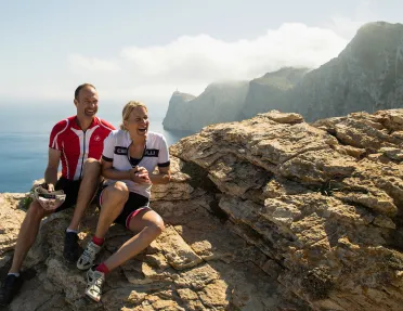 Two bikers resting on rocks cliffside in Mallorca.
