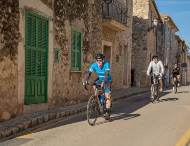 Bikers riding past stone facade houses in Spain.