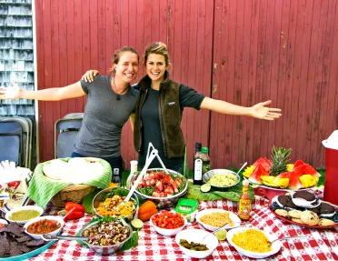 Two people posing behind lunch spread.