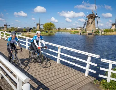 Bikers on small bridge with windmills in background